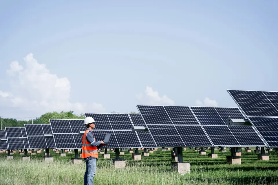 Técnico con casco revisando datos en un portátil ante una planta fotovoltaica